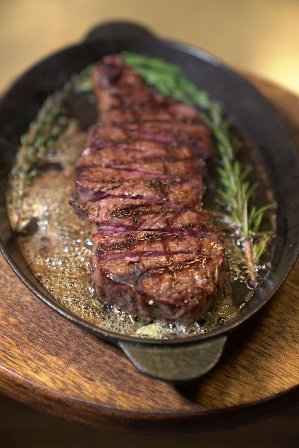 Sliced grilled steak with rosemary in a cast-iron pan